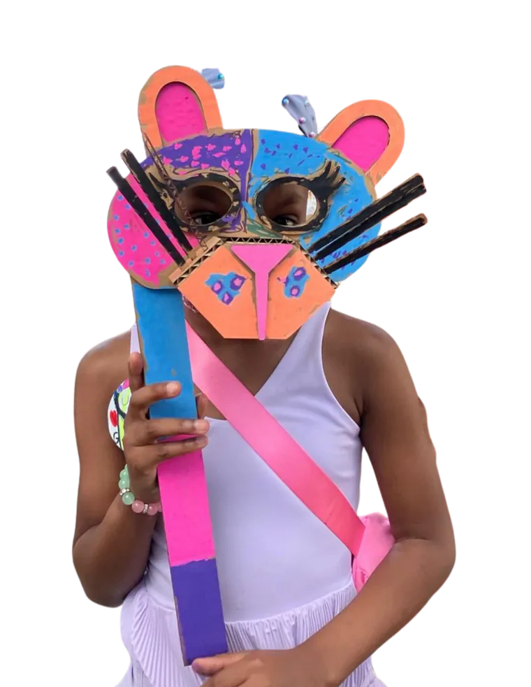 A young maker holding up a colorful cardboard jaguar mask they designed and built